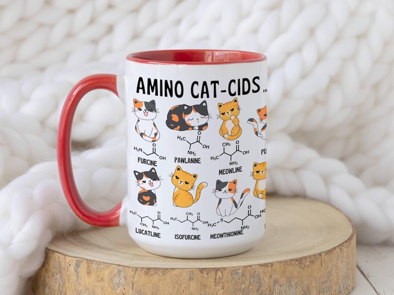 Może przedstawiać: Biały kubek ceramiczny z czerwonym rantem i uchwytem. Kubek przedstawia kresk&oacute;wkową ilustrację kot&oacute;w ze wzorami chemicznymi i tekstem "AMINO CAT-CIDS".