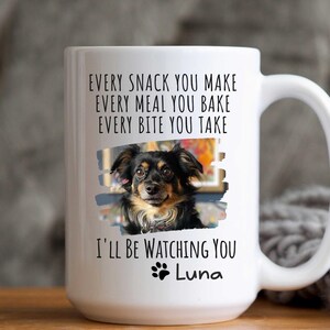 May include: White ceramic coffee mug with a black and white photo of a dog and the text "EVERY SNACK YOU MAKE EVERY MEAL YOU BAKE EVERY BITE YOU TAKE I'LL BE WATCHING YOU Luna"