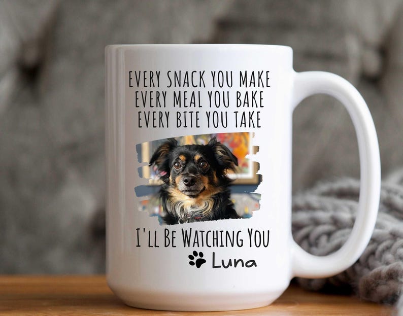 May include: White ceramic coffee mug with a black and white photo of a dog and the text "EVERY SNACK YOU MAKE EVERY MEAL YOU BAKE EVERY BITE YOU TAKE I'LL BE WATCHING YOU Luna"