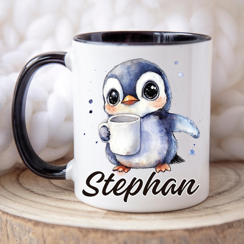 May include: White ceramic mug with a black interior and handle. The mug features a watercolor illustration of a cute penguin holding a small white cup. The name "Stephan" is written in black script on the front of the mug.