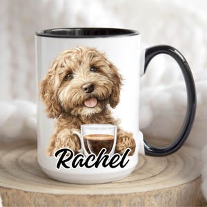 May include: White ceramic mug with a black handle and rim. It features a watercolour illustration of a brown Goldendoodle dog holding a glass of coffee. The name "Rachel" is written in a script font below the dog.