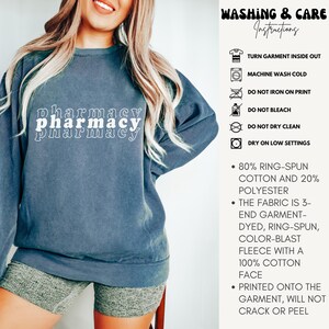 May include: A dark blue sweatshirt with the text "pharmacy" printed on it in white. The sweatshirt has a distressed look and is made of 80% ring-spun cotton and 20% polyester. The fabric is 3-end garment-dyed, ring-spun, color-blast fleece with a 100% cotton face. The print is printed onto the garment and will not crack or peel.