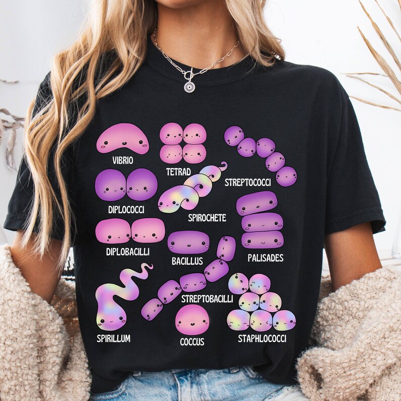 May include: Black t-shirt with a colourful illustration of different bacteria, such as Vibrio, Tetrad, and Spirochete. Each bacterium is depicted with a cute, cartoon-like design and labelled with its scientific name. The shirt is made of a soft material.