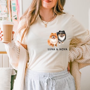 May include: A white t-shirt with a graphic of two Pomeranian dogs, one orange and one black and white. The text "LUNA & NOVA" is printed below the dogs.