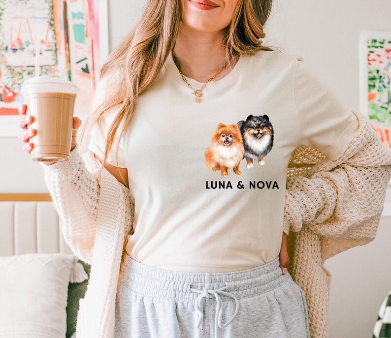 May include: A white t-shirt with a graphic of two Pomeranian dogs, one orange and one black and white. The text "LUNA & NOVA" is printed below the dogs.