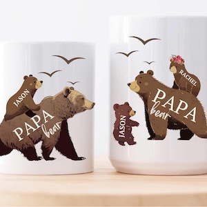 Może przedstawiać: Dwa białe ceramiczne kubki z ilustracjami brązowych niedźwiedzi. Większy kubek ma brązowego niedźwiedzia z mniejszym niedźwiedziem na grzbiecie i tekstem "PAPA bear" i "RACHEL". Mniejszy kubek ma brązowego niedźwiedzia z mniejszym niedźwiedziem na grzbiecie i tekstem "PAPA bear" i "JASON".