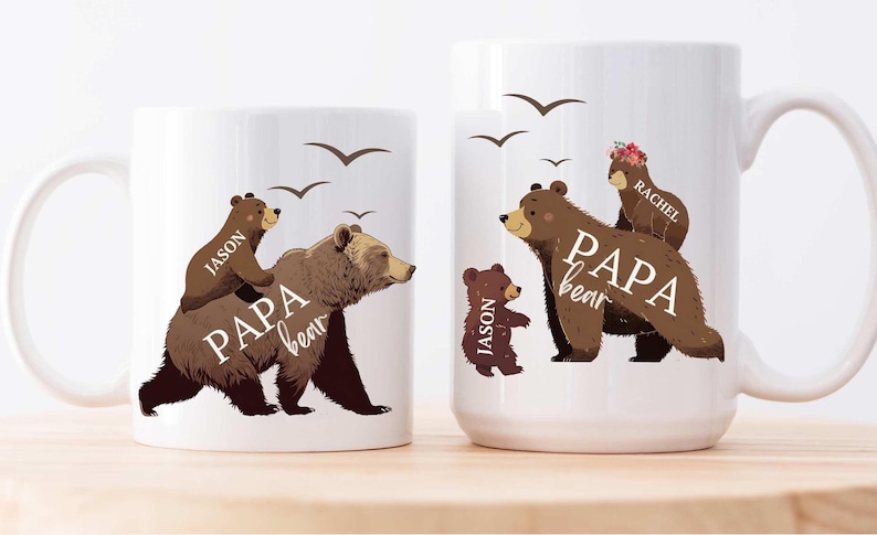 Może przedstawiać: Dwa białe ceramiczne kubki z ilustracjami brązowych niedźwiedzi. Większy kubek ma brązowego niedźwiedzia z mniejszym niedźwiedziem na grzbiecie i tekstem "PAPA bear" i "RACHEL". Mniejszy kubek ma brązowego niedźwiedzia z mniejszym niedźwiedziem na grzbiecie i tekstem "PAPA bear" i "JASON".