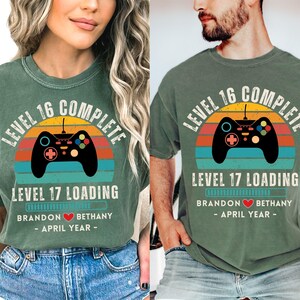 May include: A pair of green t-shirts with a retro video game controller graphic and the text "Level 16 Complete" and "Level 17 Loading". The shirts also include the text "Brandon Bethany - April Year -"