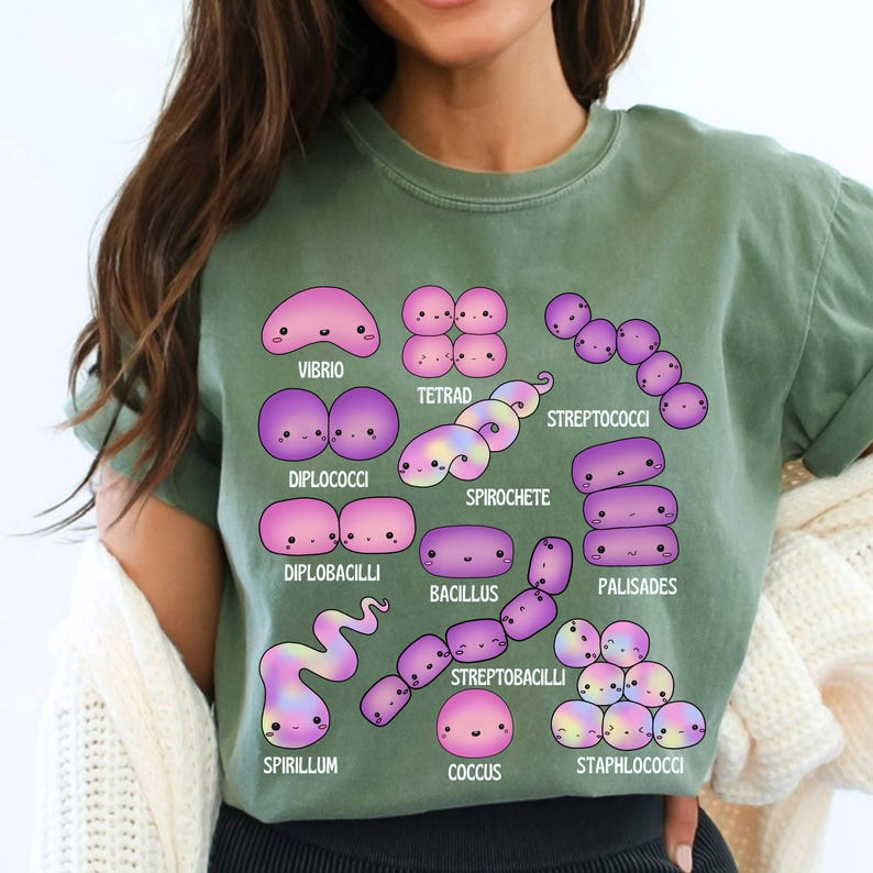 May include: Sage green t-shirt with a colourful illustration of different bacteria, such as Vibrio and Spirochete. Each bacterium is depicted with a cute, cartoon design and labelled with its scientific name. The t-shirt is made of a soft material.