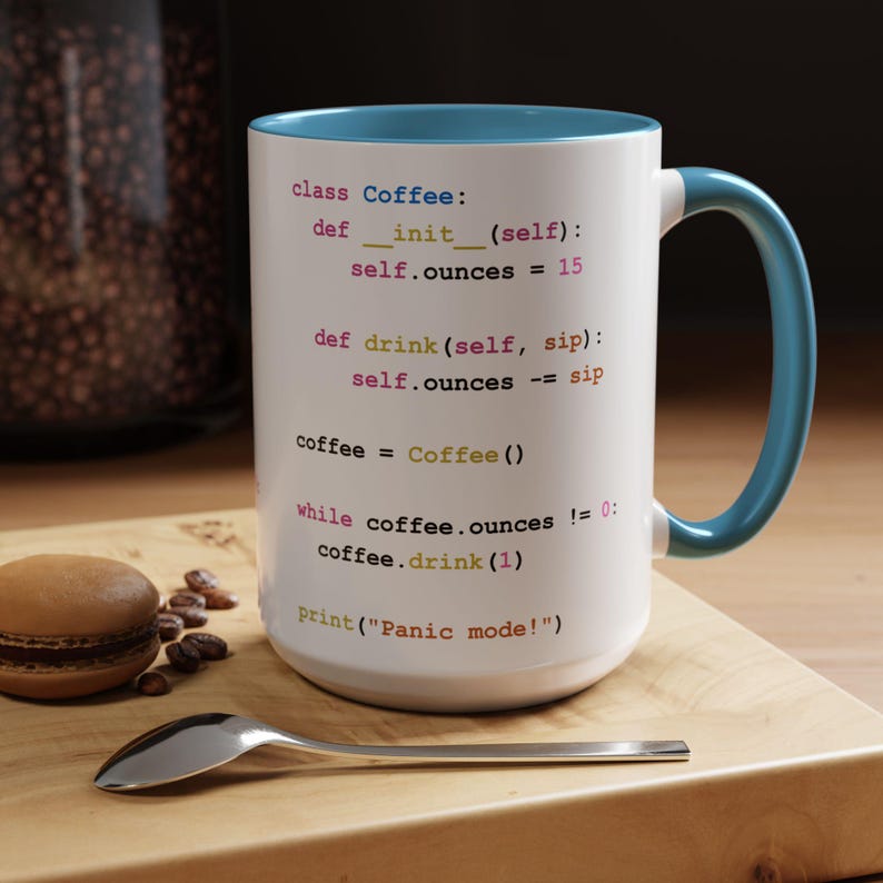 May include: White ceramic mug with a blue rim and handle. The mug features a code snippet in a light blue font that reads "class Coffee: def __init__(self): self.ounces = 15 def drink(self, sip): self.ounces -= sip coffee = Coffee() while coffee.ounces != 0: coffee.drink(1) print("Panic mode!")"
