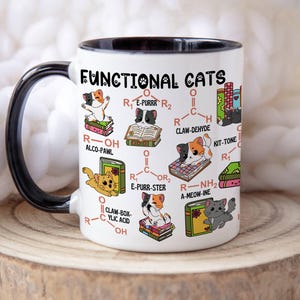 Könnte beinhalten: Weißer Keramikbecher mit schwarzem Henkel und Rand, mit dem Text "FUNCTIONAL CATS" und Illustrationen von Katzen mit wissenschaftlichen Diagrammen. Der Becher steht auf einer Holzoberfläche.