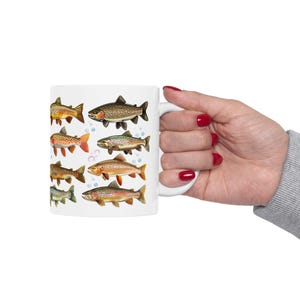 May include: White ceramic mug featuring illustrations of various fish species. The fish are depicted in a detailed, vintage style, with a range of colors including brown, orange, and green. Bubbles are also included in the design.