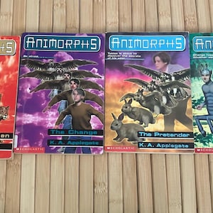 Puede incluir: Se muestran cuatro libros de Animorphs de K.A. Applegate. Las portadas presentan ilustraciones de personas y animales, con títulos como "The Forgotten", "The Change", "The Pretender" y "The Illusion". Los libros están sobre una superficie de madera.