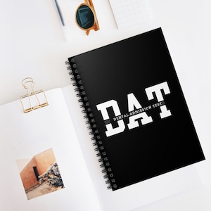 May include: A black spiral notebook with the text "DAT DENTAL ADMISSION TEST" in white letters. The notebook has a black and white stripe design.
