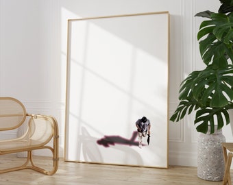 May include: A white framed canvas print with a person standing in the middle of the canvas. The person is wearing a grey shirt and black pants. The person is holding a black umbrella. The person's shadow is cast on the canvas.