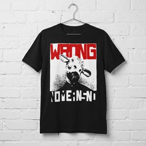 May include: A black short-sleeved t-shirt featuring a graphic print of a creature with large ears. The design includes the word WRONG in bold red letters at the top and the text NOME:N-N-NI in white letters at the bottom, all set against a white square.