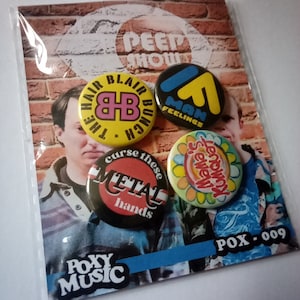May include: Set of four round button badges with various designs. The badges feature colourful graphics and text, including "The Hair Blair Bunch", "Man Feelings", "Curse These Metal Hands", and "Kumquat Sewew".