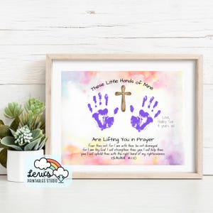 May include: Framed print featuring purple handprints and a wooden cross on a watercolor background. Text reads "These Little Hands of Mine Are Lifting You in Prayer" with a Bible verse. Signed "Love, Hadley Sue 4 years old."