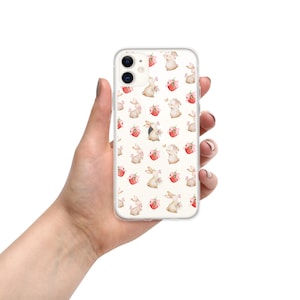 May include: A clear phone case with a white background and a repeating pattern of watercolor bunnies holding pink flowers and red baskets.