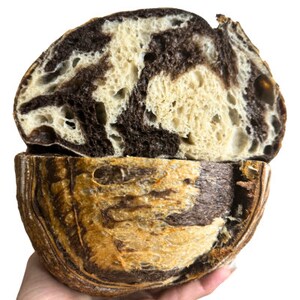 May include: A loaf of sourdough bread with a swirl of dark chocolate dough. The bread is sliced in half, revealing the marbled interior.