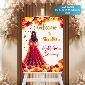 May include: Welcome sign for a half saree ceremony featuring a floral design and a woman in a red and gold saree. The sign reads "Welcome to Shruthi's Half Saree Ceremony".