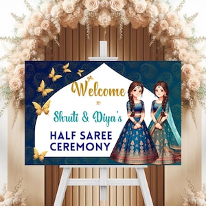 May include: A welcome sign for a Half Saree Ceremony. The sign features the text "Welcome to Shruti & Diya's Half Saree Ceremony" in gold and teal. The background is navy blue with gold butterflies and paisley patterns. Two illustrations of women in traditional attire are on the right.