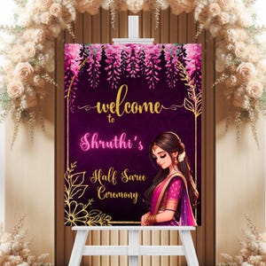 May include: Welcome to Shruthi's Half Saree Ceremony sign with a purple background, gold floral accents, and a pink and purple illustration of a woman in a saree.