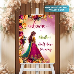 Puede incluir: Un cartel de bienvenida para una ceremonia de medio sari con un borde floral y una ilustración de dibujos animados de una mujer con un sari rosa y turquesa. El cartel dice "Bienvenido a la ceremonia de medio sari de Shruthi".