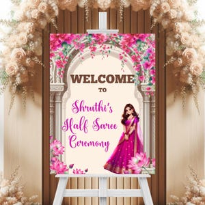 May include: Welcome to Shruthi's Half Saree Ceremony sign with a floral archway and a cartoon illustration of a woman in a pink sari.