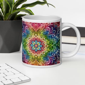 Può includere: Tazza in ceramica bianca con un design di mandala colorato che presenta un arcobaleno di colori e un fiore centrale. Il mandala è intricato e dettagliato, con una varietà di motivi e forme.