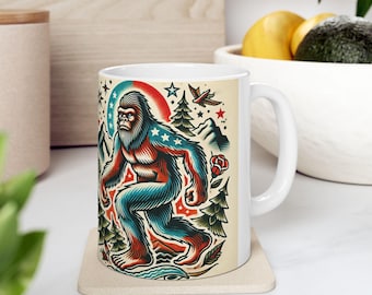May include: White ceramic mug with a colorful illustration of a Bigfoot wearing a red, white, and blue American flag pattern. The illustration is surrounded by trees, stars, and a red rose.