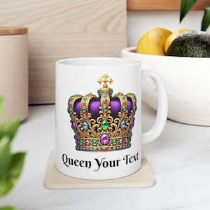 Può includere: Tazza in ceramica bianca con un design a corona dorata decorata con gioielli viola, verdi e blu. Il testo "Queen Your Text" è stampato sulla tazza.