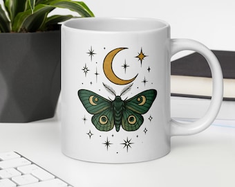 May include: White ceramic mug with a green moth and a crescent moon with stars in a celestial design.