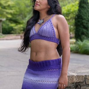 May include: A woman wearing a purple crochet top and skirt. The top and skirt are both ombre, fading from a darker purple to a lighter shade. She is wearing a silver star-shaped necklace.