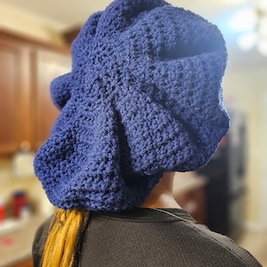 May include: A navy blue crocheted beanie with a loose, slouchy fit. The beanie is worn on a person with long, blonde hair.