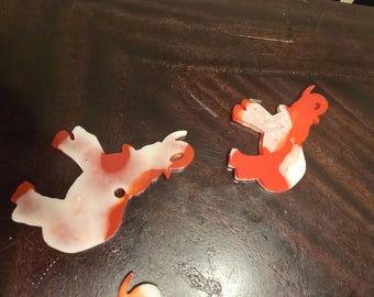 May include: Two red and white plastic elephant ornaments. The elephants are in a playful pose, with one elephant's trunk raised in the air.