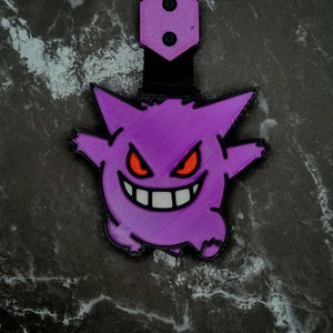 May include: Purple and white 3D printed keychain featuring a cartoon ghost with red eyes and a wide grin.