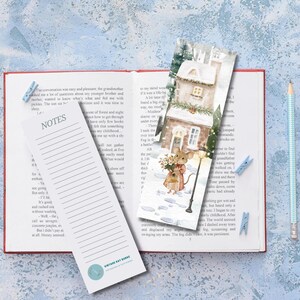 May include: An open book with a bookmark and a notepad. The bookmark features a watercolor illustration of a house and a mouse. The notepad has lined pages and the word "NOTES" at the top. A pencil and two blue paper clips are also visible.