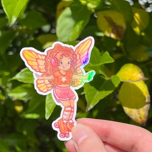 May include: A vibrant sticker of a fairy on roller skates. The fairy has orange hair, headphones, and iridescent wings. She wears a pink outfit with orange accents. The sticker is held against a backdrop of green leaves.