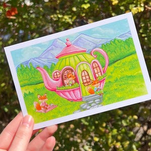 May include: A whimsical illustration of a teapot house with a pink and green exterior. Three foxes are depicted, one sitting in a window, one standing on a stone step, and one sitting on a blanket outside. The house is surrounded by green grass and trees, with mountains in the background.