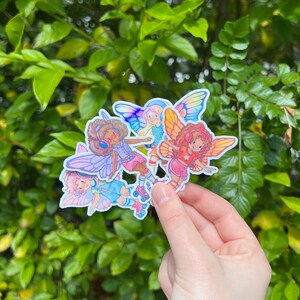 May include: A cluster of fairy stickers, each depicting a cartoon fairy with butterfly wings and roller skates. The fairies are dressed in bright outfits and have diverse skin tones and hair colours. The wings are in shades of blue, pink, and yellow.