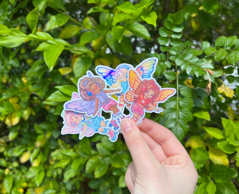 May include: A cluster of fairy stickers, each depicting a cartoon fairy with butterfly wings and roller skates. The fairies are dressed in bright outfits and have diverse skin tones and hair colours. The wings are in shades of blue, pink, and yellow.