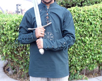 May include: Teal-colored tunic with a lace-up neckline and sleeves, featuring a white embroidered symbol on the chest. The tunic is paired with a silver sword. The sleeves have decorative ties. The tunic is made of a soft material.