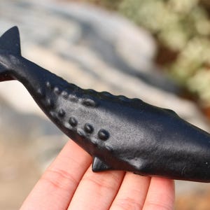 May include: A black ceramic whale figurine with a smooth, glossy finish. The whale has a detailed, textured body with raised bumps.