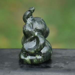 May include: A dark green jade elephant sculpture with a curled trunk and detailed carving. The figurine is smooth and polished, with variations in color. The elephant is a symbol of good luck and fortune.