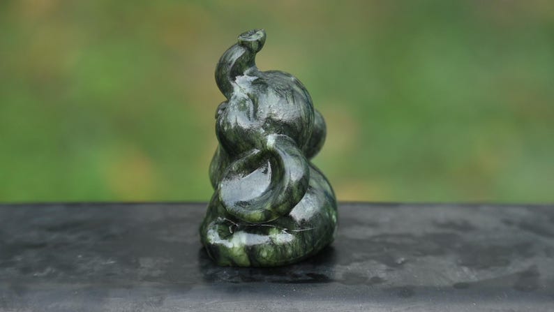May include: A dark green jade elephant sculpture with a curled trunk and detailed carving. The figurine is smooth and polished, with variations in color. The elephant is a symbol of good luck and fortune.