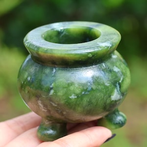 Op de afbeelding: Een kleine, groene jade wierookbrander met een afgeronde body en drie kleine voetjes. De bovenkant heeft een brede opening. De jade heeft een gevlekt patroon van licht- en donkergroen. De brander is ongeveer 6,35 cm hoog.