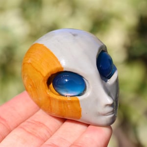 May include: A small, hand-painted, ceramic alien head sculpture with blue eyes and a yellow and grey paint scheme.