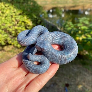 May include: A coiled blue snake figurine with a textured surface and pink accents. The snake is in a resting position, with its head raised. The figurine is a decorative item.