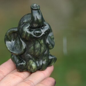 May include: A small, dark green elephant figurine with detailed carving. The elephant is in a seated position with its trunk raised. The figurine is made of a polished, possibly stone-like material.